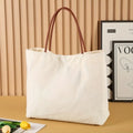 Beige white and white canvas tote bag with long handle straps.
