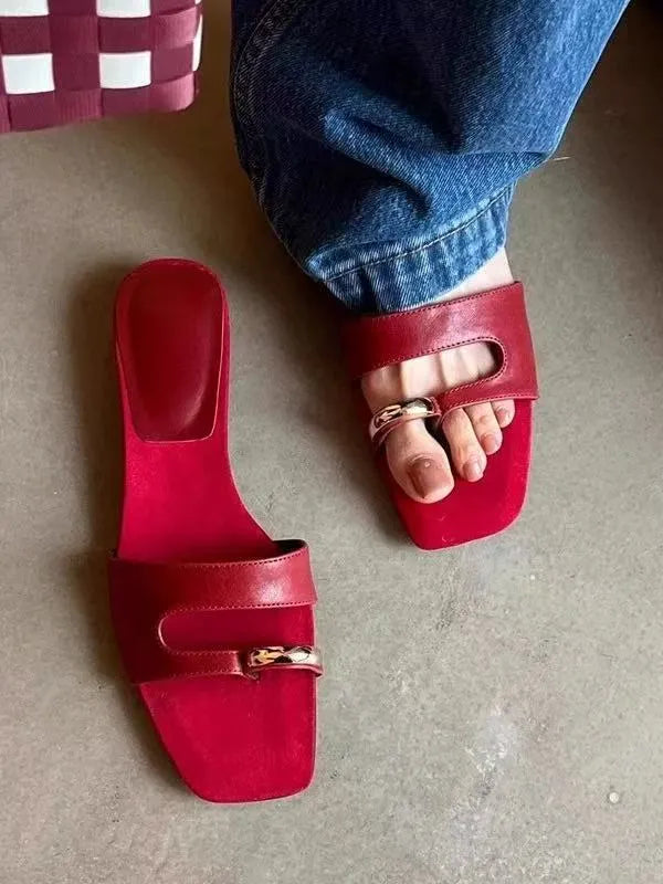 A pair of black square-toe slippers with a leather upper and light rubber sole on a wooden floor.