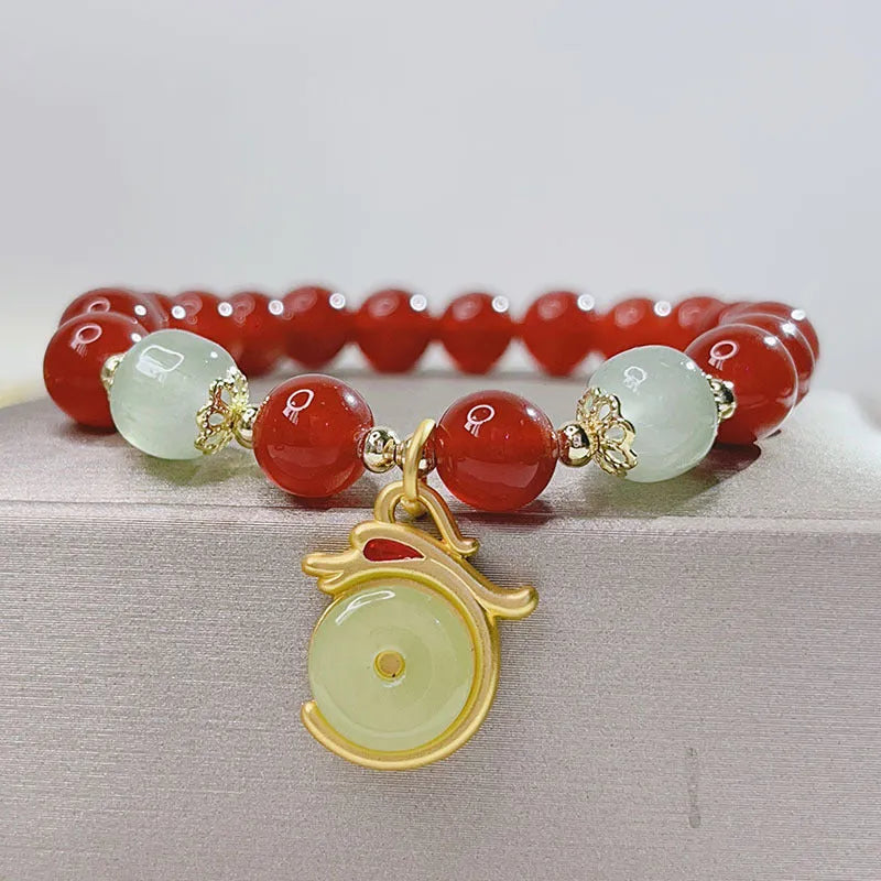 Close-up of a manually crafted red agate bracelet with Lucky Bag and dragon designs on a wrist.